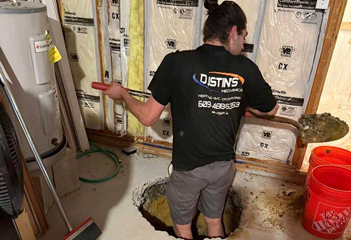 Technician from Dustin's Plumbing Heating and A/C Repair digging near a basement hole
